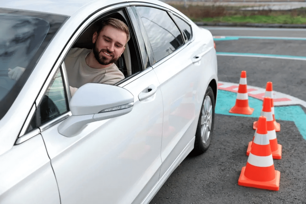 Smiling man in a white car on a driving course with orange traffic cones