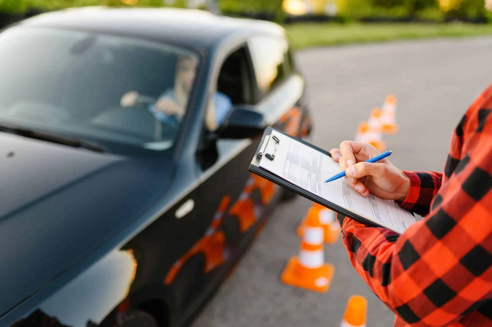 Driving instructor with a clipboard evaluating a student in a car among traffic cones