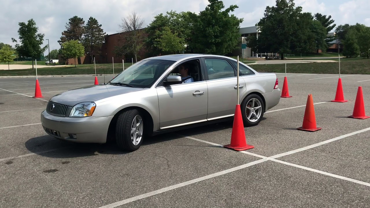 Silver sedan navigating a course of orange traffic cones in a parking lot
